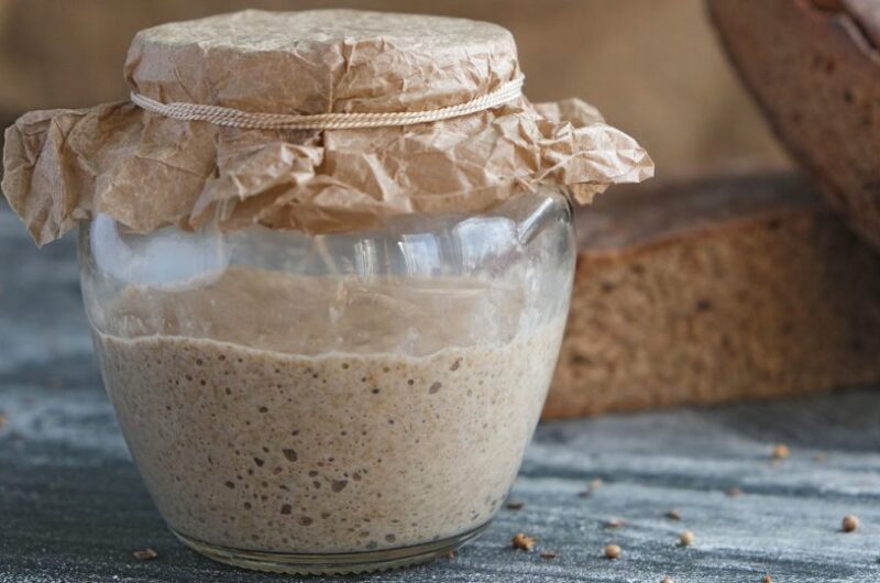 fresh rye sourdough in glass jar and loaf of whole grain bread, yeast-free leaven starter for healthy rustic handmade homemade bread, spices scattered on table